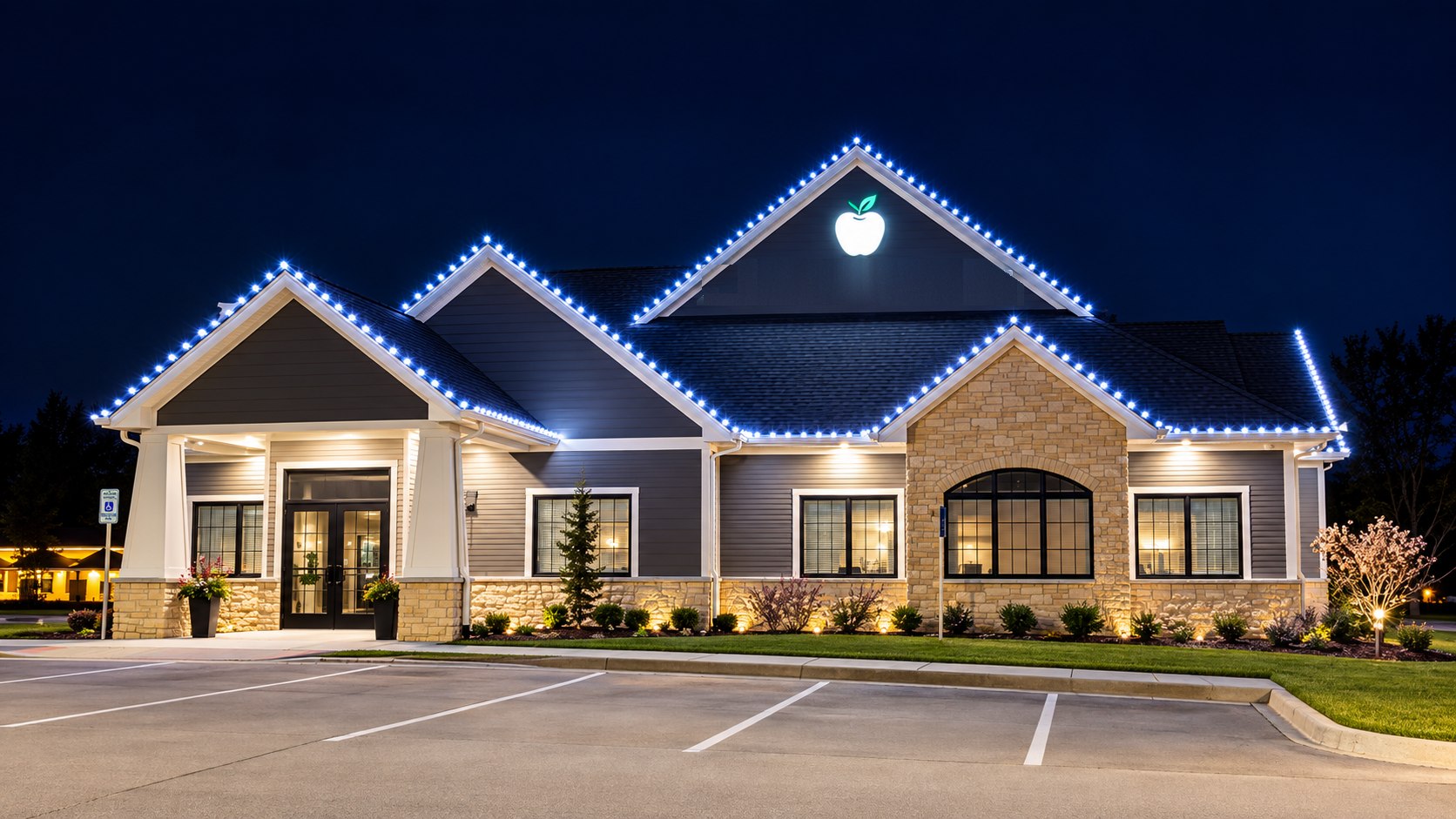 Single-story office building at night with cool white bulbs outlining every gable and roofline above a landscaped front and parking lot